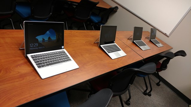 laptops lined up on a table in a classroom